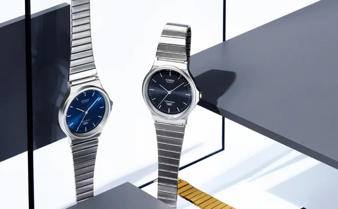 Casio metal watches with light blue and green dials showcased on a wooden surface, highlighting the brand’s new affordable color-focused collection.